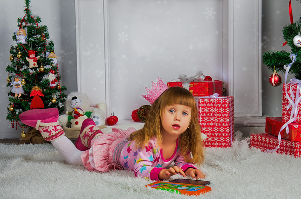 Happy little girl sitting on a chair next to the Christmas tree - Photo, Image