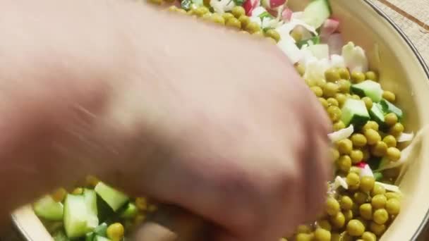  la mano de un hombre mezcla verduras picadas con guisantes enlatados en una cacerola con un cuchillo. - Metraje, vídeo