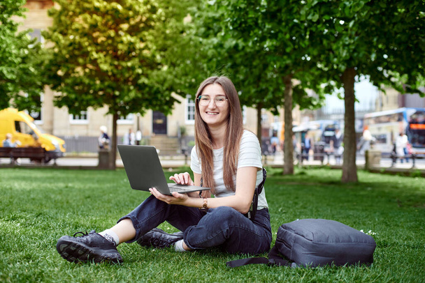 Een jonge mooie vrouw zit op het gazon voor een laptop - Foto, afbeelding