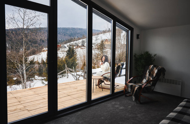Woman enjoying winter holidays on terrace of contemporary barn house in the mountains. - Fotó, kép