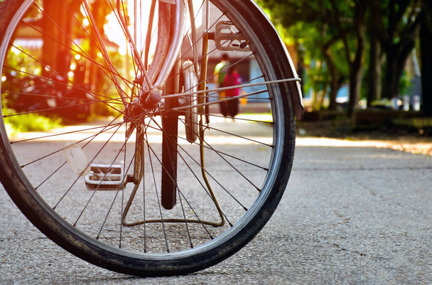 Widok z przodu przedniej opony zabytkowego roweru, który zaparkowany na wąskiej ulicy w parku publicznym, miękkie i selektywne skupienie, vintage koncepcja rowerów. - Zdjęcie, obraz