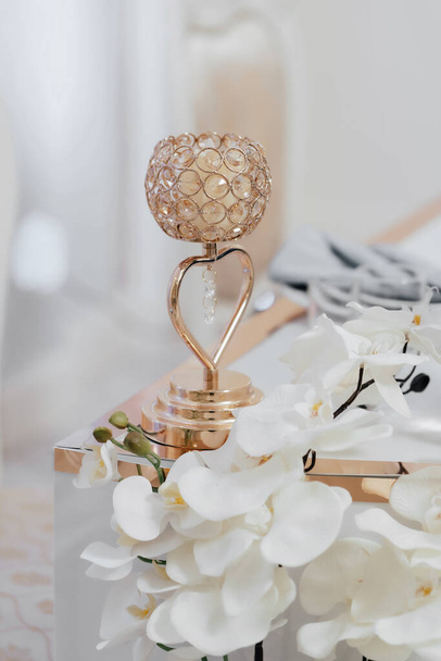 Wedding decor. On a bright table is a candlestick, with two baskets of orids light background - Fotoğraf, Görsel
