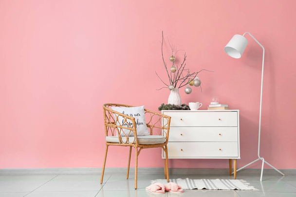 Ladekast, lamp en stoel in de buurt van roze muur in kamer ingericht voor Kerstmis - Foto, afbeelding