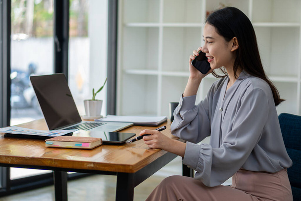 Empleada asiática que trabaja en la oficina con teléfono y computadora portátil Sam, concepto de contabilidad financiera. - Foto, imagen