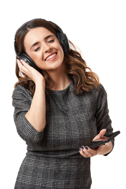 Young businesswoman with over ear headphones listening music from her smartphone and dancing, isolated on white background - Fotografie, Obrázek