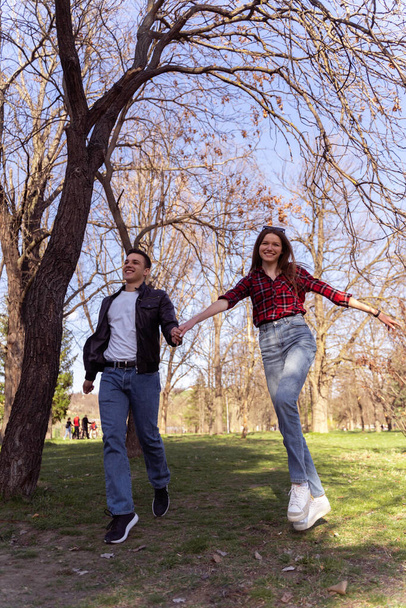 Ağacın yanındaki parkta yürüyen ve gülen sevimli bir çift. - Fotoğraf, Görsel