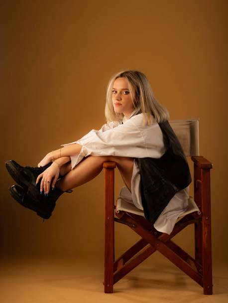 Attractive and amazing young girl is posing on the chair alone in studio on yellow background while having a fun time - Fotó, kép