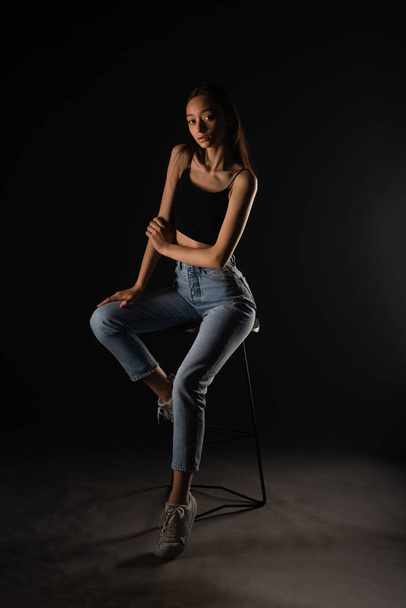 Beautiful skinny girl is posing professionally on the high chair in studio - Foto, afbeelding
