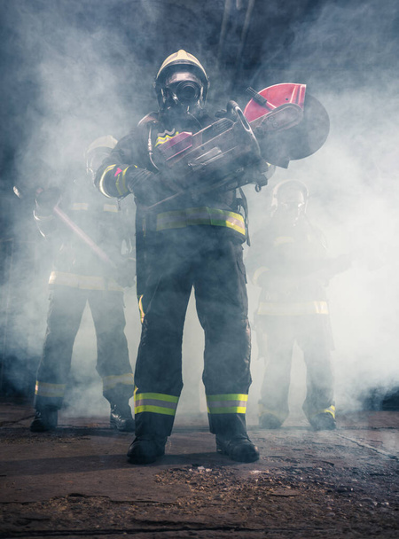 Portrait d'un pompier tenant une tronçonneuse de secours dans un garage fumé du service d'incendie - Photo, image