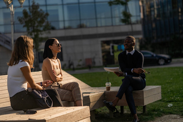 Tři multiraciální obchodníci přemýšlejí o projektu, zatímco sedí na lavičce - Fotografie, Obrázek