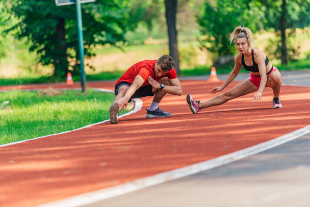 Atraente jovem casal alongamento juntos em uma pista de corrida depois de se exercitar ao ar livre - Foto, Imagem