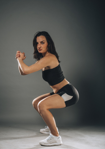 Young slim brunette fitness woman stretching on dark wall background - Фото, зображення