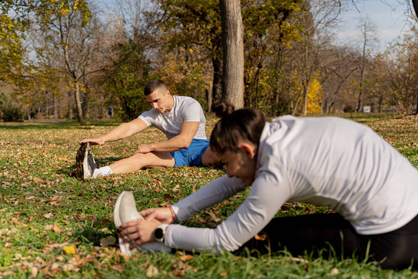 Twee aantrekkelijke en verbazingwekkende fit vrienden zijn stretching op het gras, terwijl ze samen geconcentreerd - Foto, afbeelding