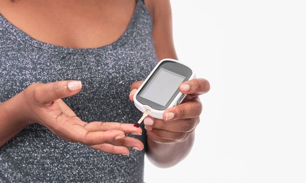 Gros plan d'une femme vérifiant le taux de sucre dans le sang avec un glucomètre numérique sur fond blanc - Photo, image