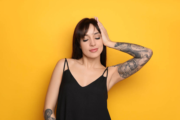 Beautiful woman with tattoos on arms against yellow background - Фото, изображение