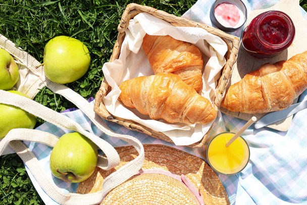 Blanket with juice, jam and croissants for picnic on green grass, flat lay - Φωτογραφία, εικόνα