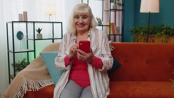 Старший старий бабуся працює на мобільному телефоні, надсилає повідомлення, здійснює онлайн покупки на домашньому дивані
 - Фото, зображення