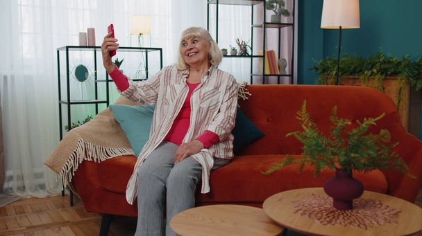 Glückliche Senioren-Großmutter hält Smartphone in der Hand und schaut sich Handy-Videotelefonie im Internet an und macht Selfie nach Hause - Foto, Bild