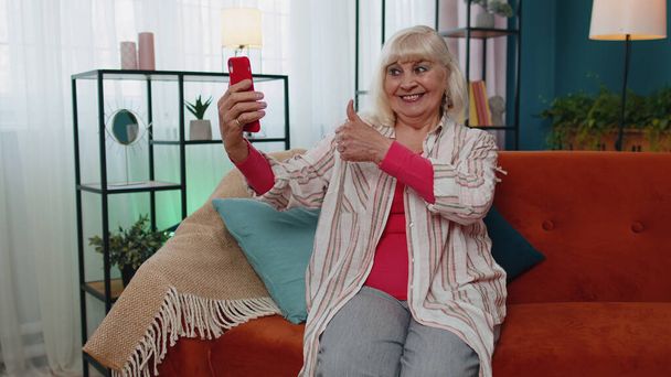 Ευτυχισμένη γιαγιά κρατώντας smartphone βλέποντας κινητό βίντεο καλώντας online κάνοντας selfie σπίτι - Φωτογραφία, εικόνα
