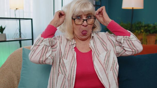 Senior old grandmother making silly facial expressions and grimacing, fooling around, showing tongue - Фото, изображение