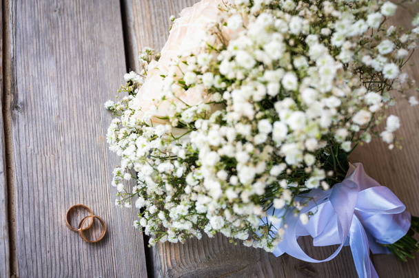 Esküvői nap beállítása egy csokor a menyasszony fehér virágok, a menyasszony és a jegygyűrűk egy fa felületen, közelkép - Fotó, kép