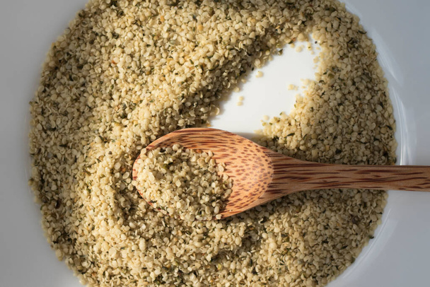 Hemp Seeds in a White Plate with a Wooden Spoon. The sun shines on the seeds. - Photo, Image