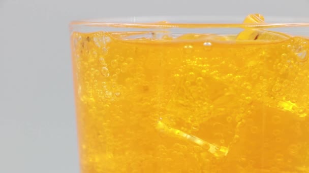 Pomarańczowa woda gazowana z lodem w szkle na białym tle. - Materiał filmowy, wideo