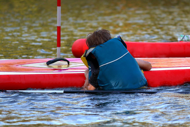 Τα παιδιά ανεβαίνουν σε κουπιά SUP σκάφους (paddleboard) στη λίμνη. Stand up κουπί επιβίβασης - φοβερό ενεργό υπαίθρια αναψυχή. - Φωτογραφία, εικόνα