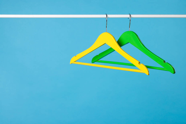 Bright clothes hangers on metal rail against light blue background. Space for text - Фото, изображение