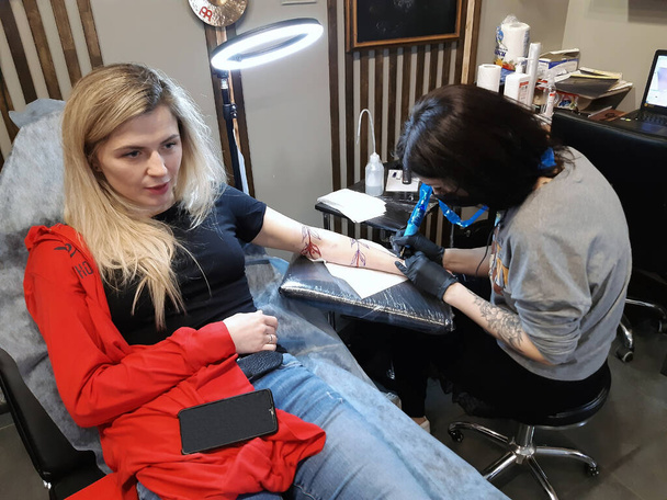 Молода приваблива блондинка влаштовує татуювання на руці в татуювальному салоні. - Фото, зображення