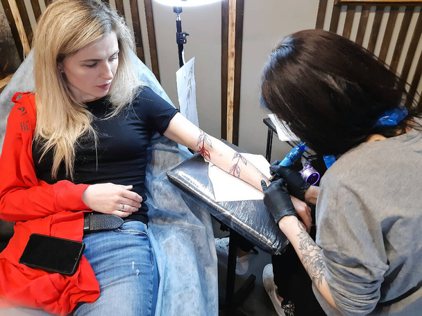 Giovane donna bionda attraente che si fa un tatuaggio sul braccio in un salone di tatuaggi - Foto, immagini