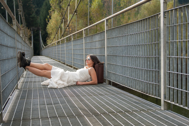 A girl with suitcase rests on the bridge - Foto, imagen