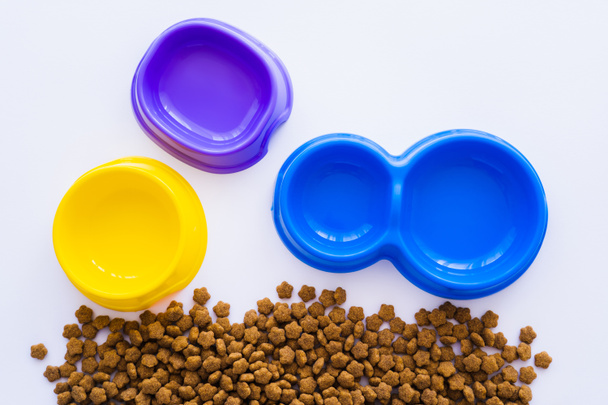 vista superior de cuencos de plástico de colores cerca de alimentos para mascotas aislados en blanco - Foto, Imagen