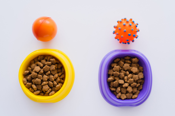 top view of rubber toys near bowls with pet food on white - Фото, зображення