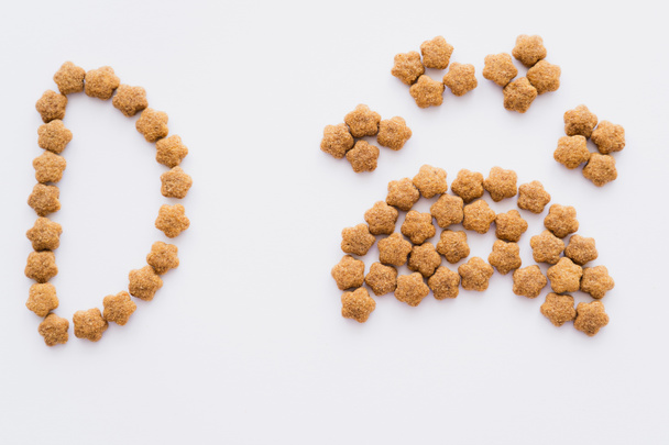 vue de dessus de la forme de patte en nourriture sèche pour animaux de compagnie près de lettre isolée sur blanc - Photo, image