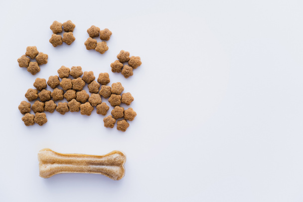 top view of paw shape made of dry pet food near bone isolated on white - Valokuva, kuva