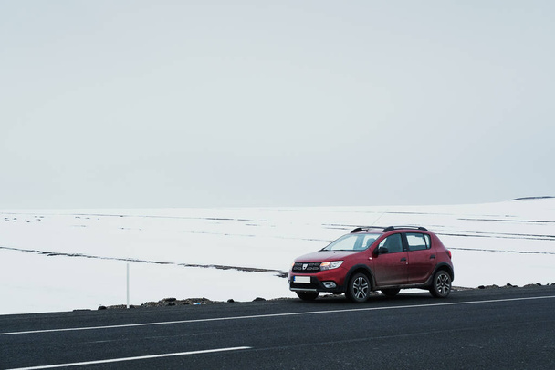 Kars, Turkey - February 25, 2022: Front and side view of a red colored Dacia brand Sandero model car paused on an asphalt road with a snowy background. - 写真・画像