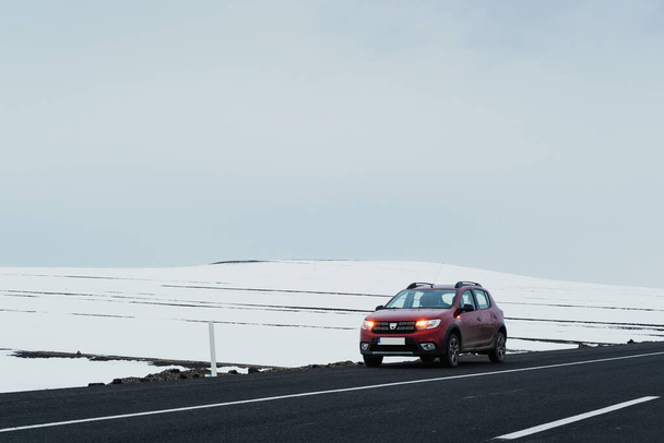 Kars, Turkey - February 25, 2022: Front and side view of a red colored Dacia brand Sandero model car paused on an asphalt road with a snowy background. - 写真・画像