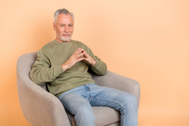 Photo of strict elder grey hairdo man sit wear pullover jeans isolated on beige background - Zdjęcie, obraz
