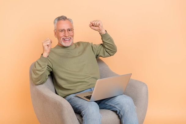 Photo of cool elder grey hairdo man sit with laptop wear eyewear pullover jeans isolated on beige background - Foto, Bild