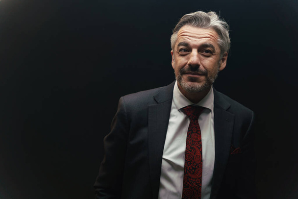 Портрет привлекательного бизнесмена в костюме, стоящем под светом на тёмном фоне. - Фото, изображение
