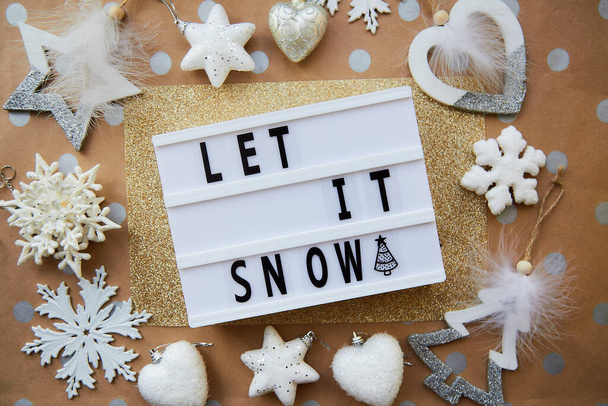 Lassen Sie es schneien Text mit Weihnachtsschmuck. Weihnachtsdekoration auf beigem und goldenem Hintergrund. Ansicht von oben - Foto, Bild