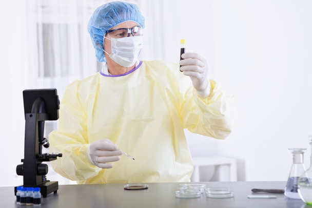 врач в защитном снаряжении держит образец крови
 - Фото, изображение