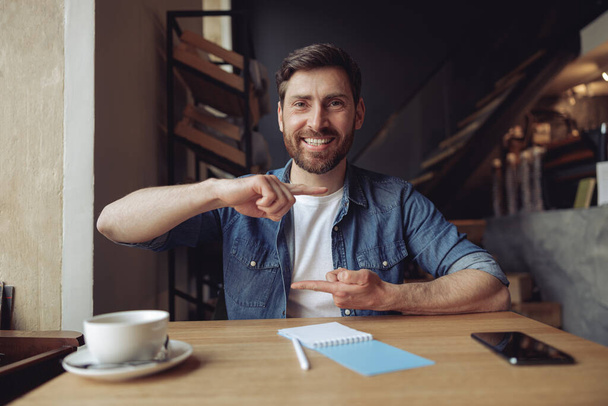 Πορτρέτο του χαρούμενος νεαρός όμορφος άνδρας δείχνει σχήμα και το μέγεθος με τα δάχτυλα στο καφέ. - Φωτογραφία, εικόνα