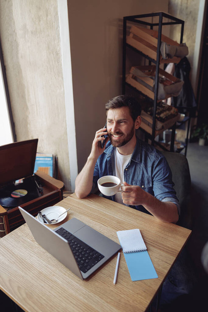 Top view valkoihoinen komea mies puhuu matkapuhelimella istuessaan kahvia ja kannettavaa tietokonetta. - Valokuva, kuva