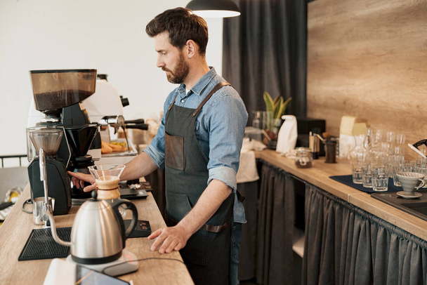 Barista guapo muele granos de café en coffeemachine - Foto, imagen
