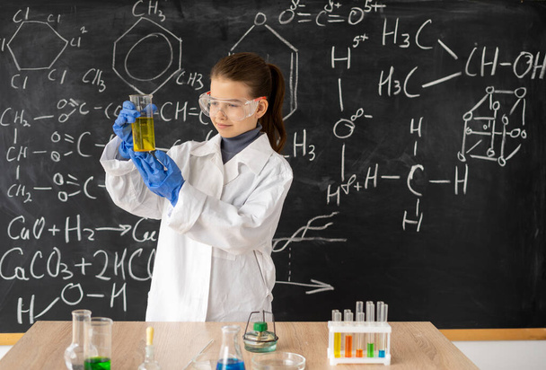 Hauska pikkutyttö tekemässä kokeita laboratoriossa. liitutaulu kemiallisten kaavojen luokassa. Tiede ja koulutus. nesteiden kokeilu kemian laboratoriossa - Valokuva, kuva