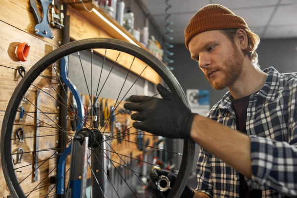 Young cycling mechanic check bicycle wheel spoke - Foto, Imagen