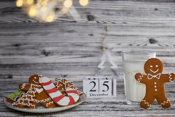 木製のヴィンテージテーブルの上に新鮮な手作りのベーキングクッキーとミルクのガラス。ふわふわトレンディーなクリスマスの装飾やカレンダー。審美的な雰囲気。かわいいクリスマスの伝統:サンタのためのミルク。スペースのコピー. - 写真・画像
