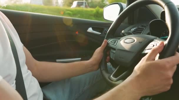 Man rijdt in een close-up auto. Stralen van de ondergaande zon schijnen door het raam - Video